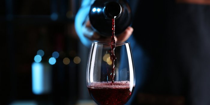 bartender pouring red wine from bottle into glass indoors, closeup