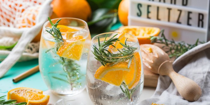hard seltzer cocktail with orange, rosemary and ice on a table summer refreshing beverage, drink with trendy zero waste a...