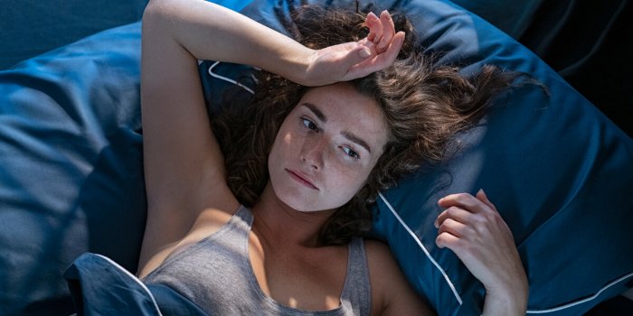 young stressed woman lying on bed late at night suffering from insomnia, sleep apnea or stress top view of depressed girl...