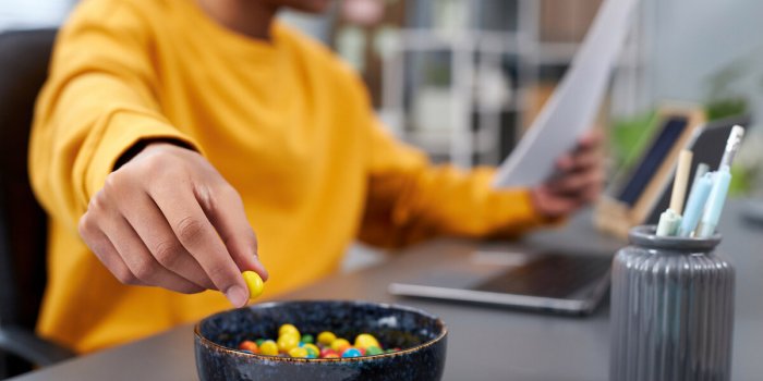 close up of young man eating snacks while working or studying at home, focus on hand holding colorful candy, copy space