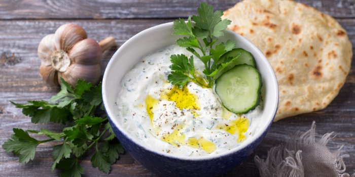 traditional greek yogurt tzatziki sauce with cucumbers and herbs on wooden background, space