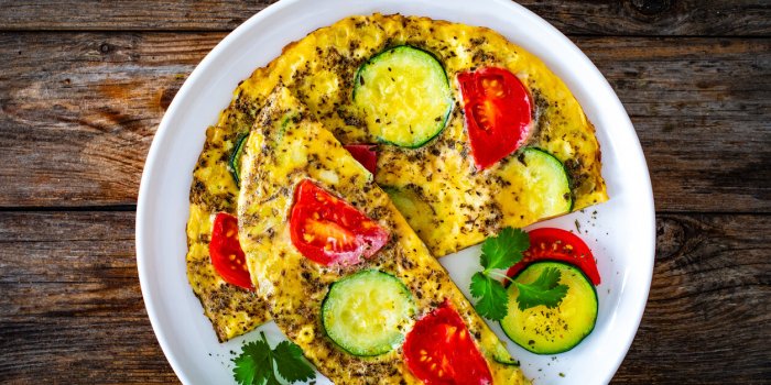 omelette - scrambled eggs with cheese, zucchini and tomatoes on wooden background