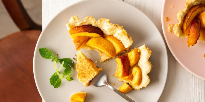 delicious piece of pie from shortcrust pastry with peach on a plate with a fork, top view on a table with a plate, baked ...