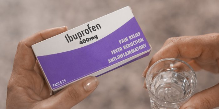 woman hold a box of 400mg ibuprofen tablets in her hand and a glass of water