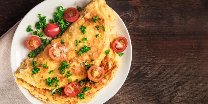 a photo of an omelet with cherry tomatoes, parsley and grated cheese, shot from above on a rustic wooden texture with a p...