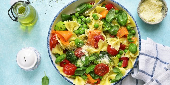 pasta primavera with spring vegetables in a white vintage bowl on a light blue slate, stone or concrete backgroundtop view