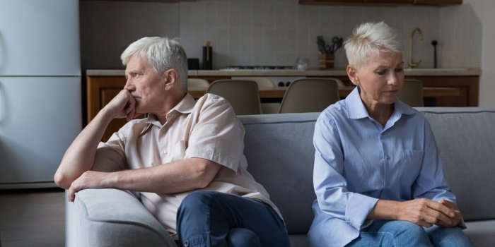 serious thoughtful unhappy older 60s wife and husband sit on couch separately couple experiencing marriage crisis, lack o...
