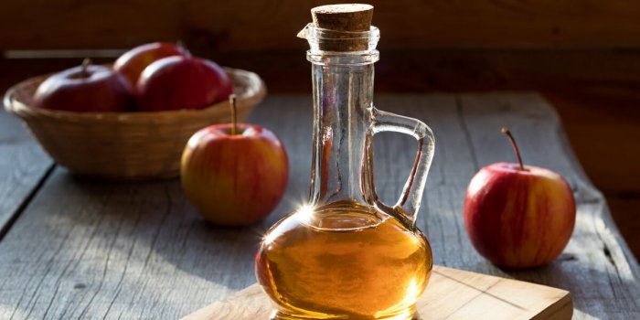 a bottle of apple cider vinegar in the morning sun, with apples in the background