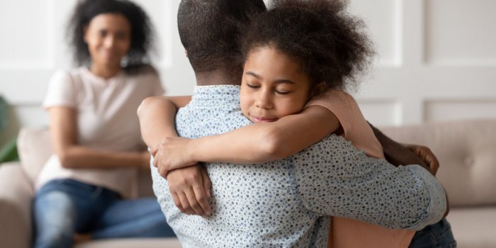 young african american man holding, embracing, comforting smiling happy calm black cute kid daughter, blurred mother sitt...