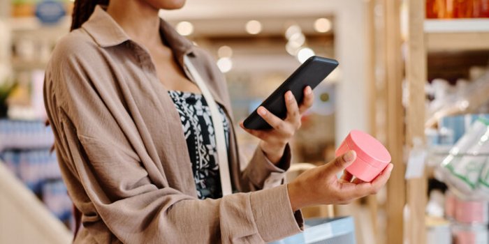 close-up of young woman making photo of cream on her smartphone during shopping in the store