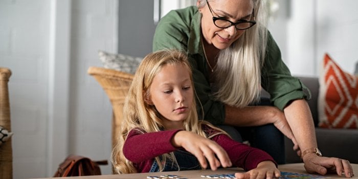 concentrated little girl doing jigsaw puzzle with old grandmother at home cute little granddaughter playing puzzle at the...