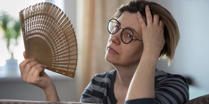 exhausted middle aged woman waving her fan, suffering from menopausal symptoms, experiencing hot flush