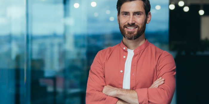 portrait of a happy and smiling programmer in the middle of a modern office, a man in glasses and a red shirt is looking ...