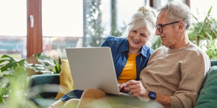 senior couple using laptop while sitting on sofa in living room at home