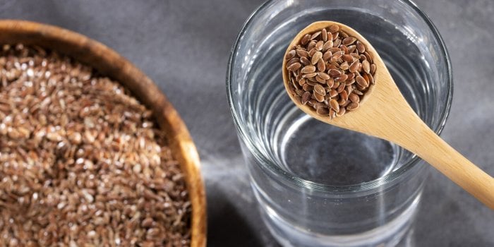 linum usitatissimum - spoon with organic flaxseeds and glass of filtered water