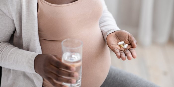 prenatal vitamins and supplements unrecognizable black pregnant woman taking pills capsules and glass of water, using med...
