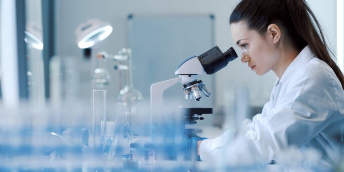 young female researcher working in the lab, she is examining the samples under a microscope