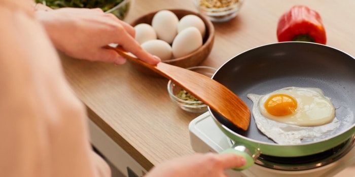 warm-toned close up of unrecognizable young woman cooking eggs on frying pan while preparing healthy breakfast in morning...