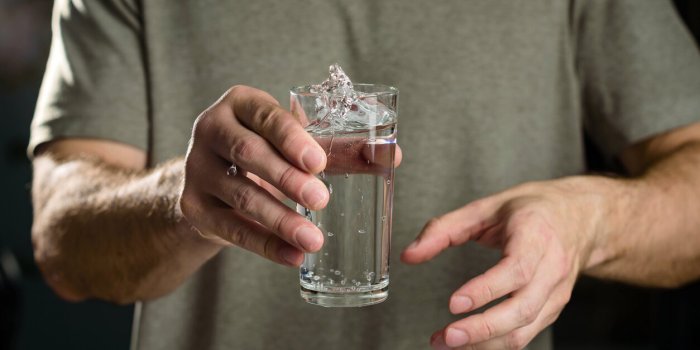 tremor of the hands when trying to drink water splashes from a glass in the hand of a man with tremors, parkinson's disease