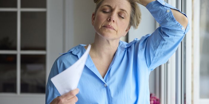 menopausal mature woman having hot flush at home cooling herself with letters or documents