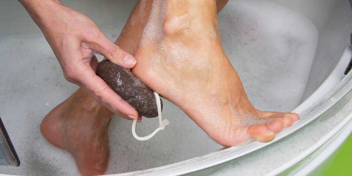 young woman exfoliating her dry skin heel with a natural pumice stone