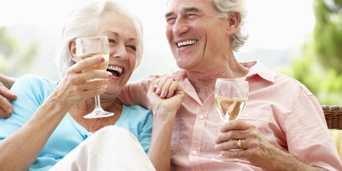 senior couple sitting on outdoor seat together drinking wine laughing