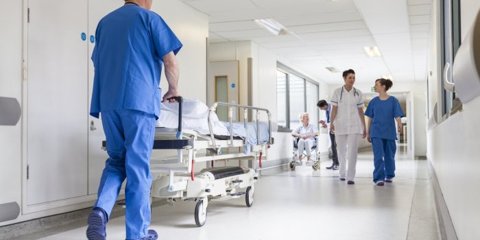 male nurse pushing stretcher gurney bed in hospital corridor with doctors & senior female patient