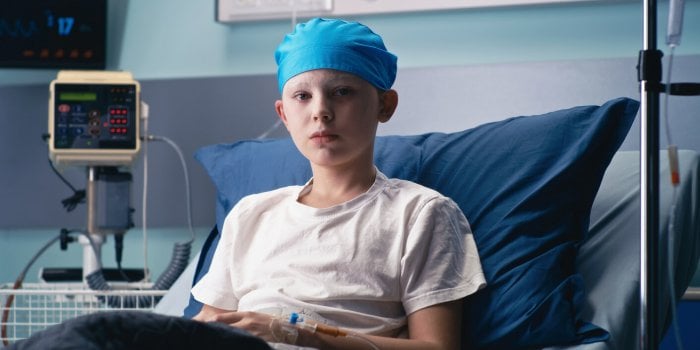 boy in hat looking at camera while lying on bed in ward of modern cancer hospital