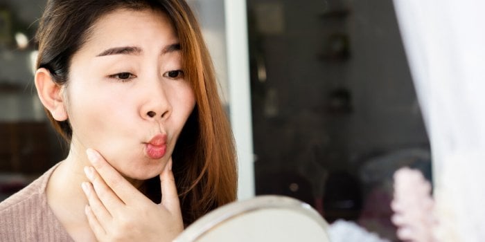 asian woman doing face yoga , exercises for anti-aging, slimming face in front of mirror