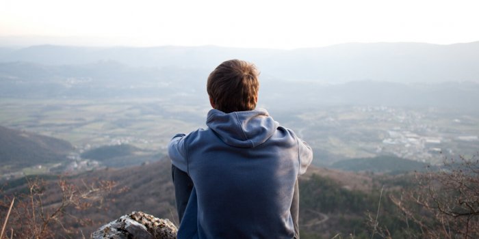 young man looking at the view and sitting on a rock copyspace above the horizon