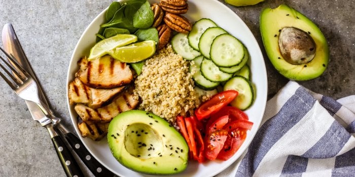 healthy salad bowl with quinoa, tomatoes, chicken, avocado, and spinach on concrete background top view