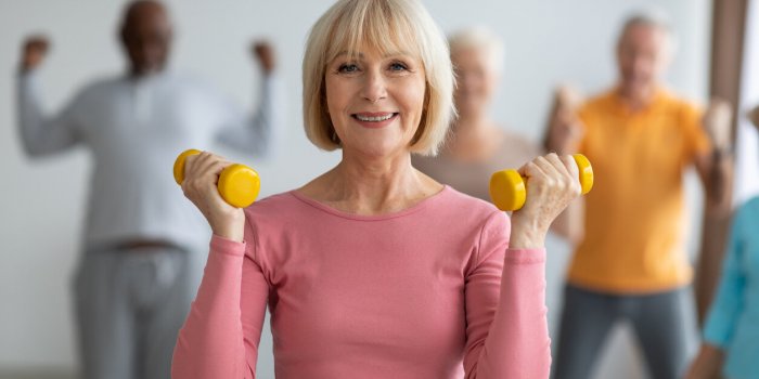 selective focus on cheerful senior lady posing with fitness tools, multiracial group of healthy elderly people in sportsw...