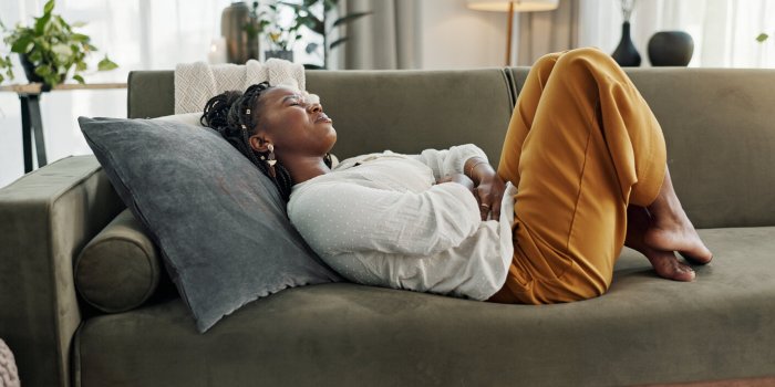 home, pain and black woman on a couch, cramps and stomach with sickness, suffering and disease in the living room african...