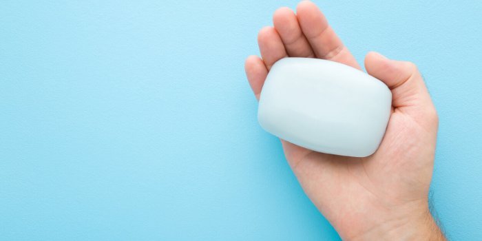 young adult man opened palm holding natural soap on light blue table background pastel color care about clean and soft bo...