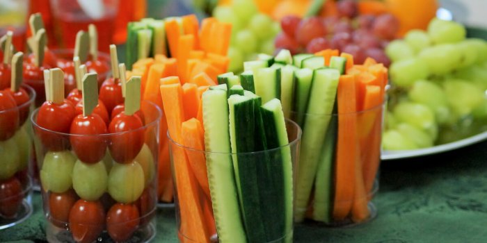 snacks of fresh fruits and vegetables including carrots, cucumbers, tomatoes and grapes on a table at a children’s party